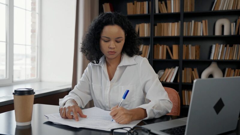 A professional woman in an office, meticulously reviewing and marking documents, highlighting the importance of quality assurance in workflow