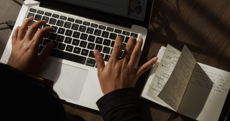 A person using a laptop outdoors, cross-referencing information in a notebook, showcasing the diligence and accuracy required in professional translation services