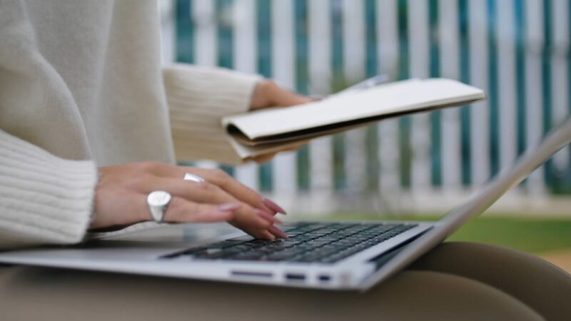 A close-up of hands typing on a laptop, with a notepad in the background, symbolizing research and staying informed about industry advancements